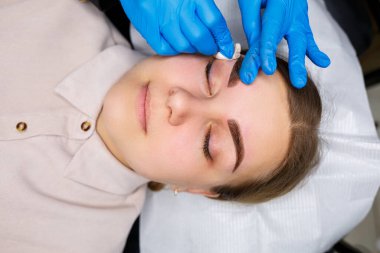 Kaşlarında kalıcı makyaj dövmesi olan bir kadın. Güzellik uzmanı kaşların bir taslağını çiziyor. Profesyonel makyaj ve estetik cilt bakımı.