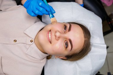 Kaşlarında kalıcı makyaj dövmesi olan bir kadın. Yakın plan güzellik uzmanı makyajı bir temele uygular. Profesyonel makyaj ve estetik cilt bakımı.