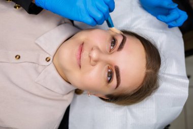 Kaşlarında kalıcı makyaj dövmesi olan bir kadın. Yakın plan güzellik uzmanı makyajı bir temele uygular. Profesyonel makyaj ve estetik cilt bakımı.