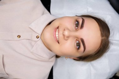 Kaşlarında kalıcı makyaj dövmesi olan bir kadın. Yakın plan güzellik uzmanı makyajı bir temele uygular. Profesyonel makyaj ve estetik cilt bakımı.