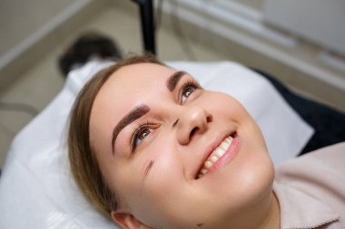 Kaşlarında kalıcı makyaj dövmesi olan bir kadın. Yakın plan güzellik uzmanı makyajı bir temele uygular. Profesyonel makyaj ve estetik cilt bakımı.