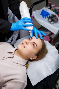 Yüzünde kalıcı makyajın lazerle çıkarılması. Dövme yaptıran genç bir kadının yakın çekimi. Yüzündeki doğal kusurların düzeltilmesi.