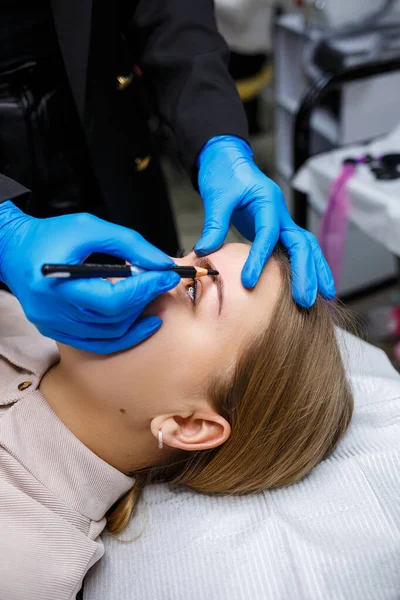 Makyaj sanatçısı, kaş kalemi olan genç bir kızın kaşlarına bir çizim uygular. Profesyonel makyaj ve estetik cilt bakımı.