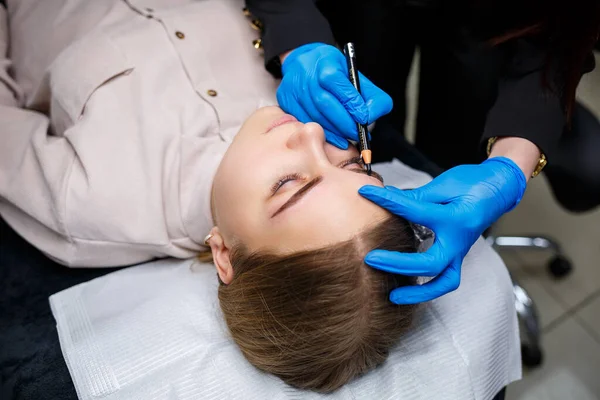 Makyaj sanatçısı, kaş kalemi olan genç bir kızın kaşlarına bir çizim uygular. Profesyonel makyaj ve estetik cilt bakımı.