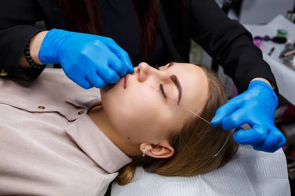 Woman with permanent makeup tattoo on her eyebrows. Close-up beautician makes a sketch of the eyebrows. Professional make-up and cosmetic skin care.