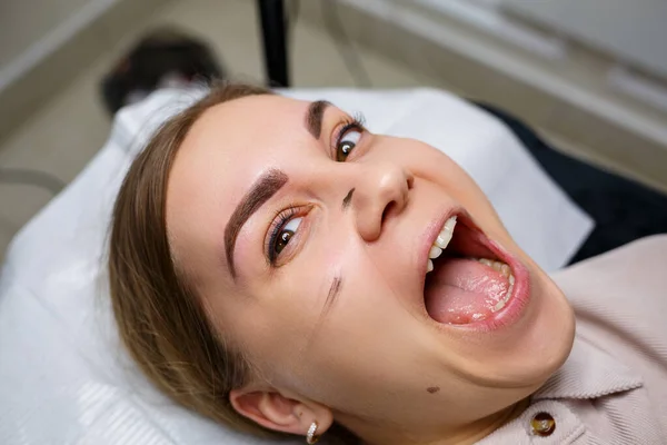 Woman with permanent makeup tattoo on her eyebrows. Close-up beautician makes makeup applies a foundation. Professional make-up and cosmetic skin care.