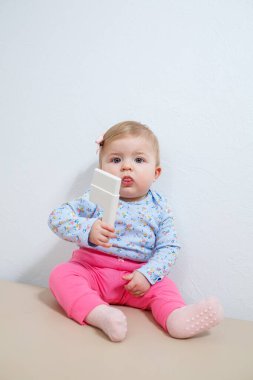 Sekiz aylık küçük bir kız, elinde kulak delici bir aletle kanepede oturuyor. Küçük çocuklar için güzellik