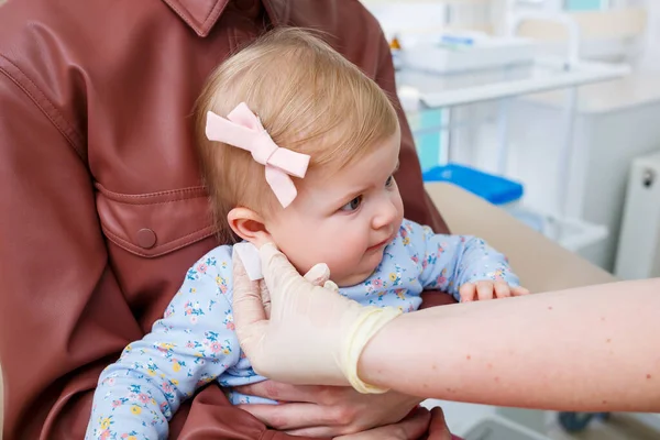 A nurse doctor pierces the ears of a little girl eight months old. Beauty for young children