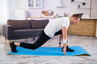 Tişörtlü kaslı atletik adam evde ısınma egzersizi yapıyor. Karantina döneminde evde spor yapıyor. Spor salonunun dışında spor salonu