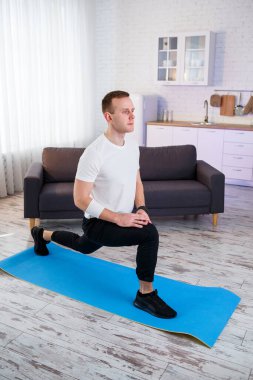 Tişörtlü kaslı atletik adam evde ısınma egzersizi yapıyor. Karantina döneminde evde spor yapıyor. Spor salonunun dışında spor salonu