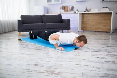 Tişörtlü yakışıklı kaslı adam evde zeminde egzersiz yapıyor. - Evet. Evde fitness var. Sağlıklı yaşam tarzı.