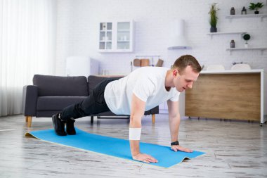 Tişörtlü yakışıklı kaslı adam evde zeminde egzersiz yapıyor. - Evet. Evde fitness var. Sağlıklı yaşam tarzı.