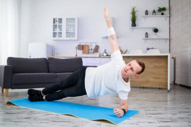Tişörtlü yakışıklı kaslı adam evde yerde fonksiyonel egzersizler yapıyor. Evde fitness var. Sağlıklı yaşam tarzı.