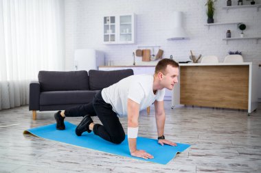 Tişörtlü yakışıklı kaslı adam evde yerde fonksiyonel egzersizler yapıyor. Evde fitness var. Sağlıklı yaşam tarzı.