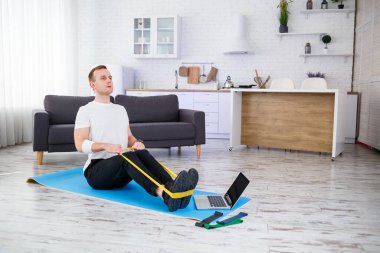 Online eğitim. Genç adam spor yapıyor. Spor lastikleriyle evde özel ders veriyor. Boş yer var. Evde spor yapıyorum.