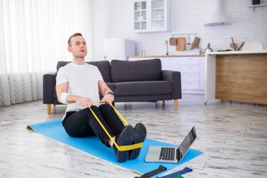 Online eğitim. Genç adam spor yapıyor. Spor lastikleriyle evde özel ders veriyor. Boş yer var. Evde spor yapıyorum.