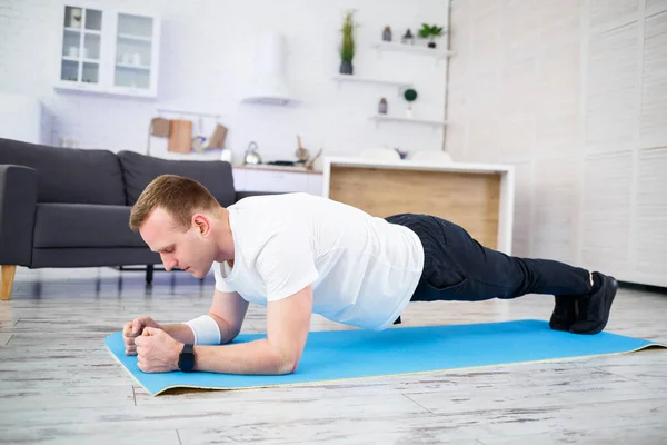 Handsome muscular man in a t-shirt is doing functional exercises on the floor at home. Fitness at home. Healthy lifestyle.