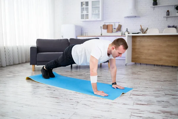 Handsome muscular man in a t-shirt doing functional plank exercises on the floor at home. Fitness at home. Healthy lifestyle.