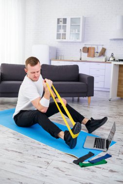 Online eğitim. Evde lastik bantlarla egzersiz yapan bir adam, boş alan. Evde spor yapıyorum.