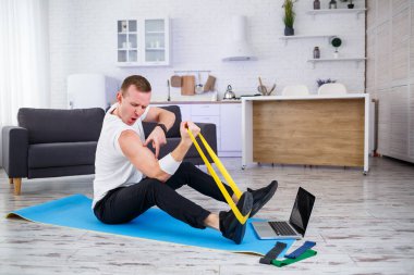 Online eğitim. Evde lastik bantlarla egzersiz yapan bir adam, boş alan. Evde spor yapıyorum.