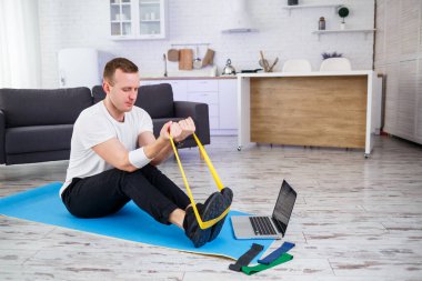 Online eğitim. Evde lastik bantlarla egzersiz yapan bir adam, boş alan. Evde spor yapıyorum.