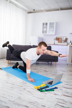 Tişört giyen sportif bir adam, iç mimarisi olan geniş ve parlak dairesinde spor yapmak için evine gider. İnternet sporları