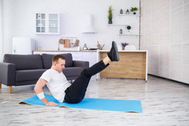 Tişört giyen güçlü bir atletik adam ve evinde iç mimarisi olan ferah ve parlak dairesinde basın egzersizleri yapıyor. Evde spor yapıyorum..