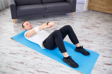 Tişört giyen güçlü bir atletik adam ve evinde iç mimarisi olan ferah ve parlak dairesinde basın egzersizleri yapıyor. Evde spor yapıyorum..