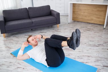 Tişört giyen güçlü bir atletik adam ve evinde iç mimarisi olan ferah ve parlak dairesinde basın egzersizleri yapıyor. Evde spor yapıyorum..