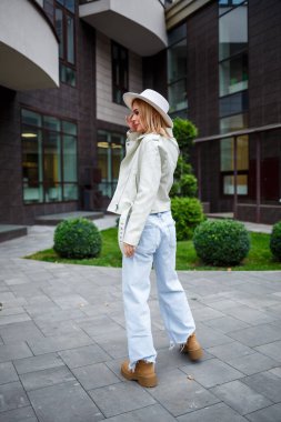 Güzel, genç ve serbest bir kadın. Güzel, şık giysiler içinde. Arka planda bir ofis binasında yürüyor.