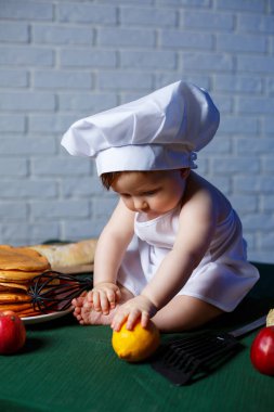 Önlük giymiş güzel bir çocuk, çocuk pişirme kostümü. Masada krep ve taze hamur işleri var.