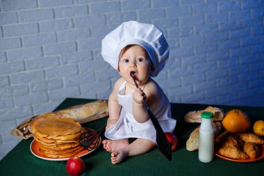 Önlük giymiş güzel bir çocuk, çocuk pişirme kostümü. Masada krep ve taze hamur işleri var.