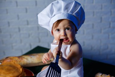 Önlük giymiş güzel bir çocuk, çocuk pişirme kostümü. Masada krep ve taze hamur işleri var.