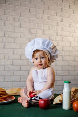 Mutfakta aşçı gibi giyinmiş küçük bir çocuk. Önlük giymiş, elma yiyen yakışıklı çocuk.