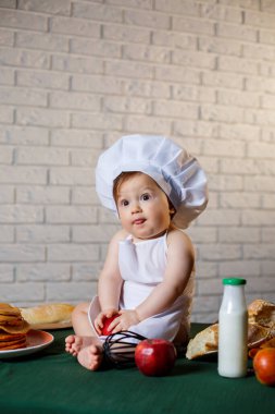 Mutfakta aşçı gibi giyinmiş küçük bir çocuk. Önlük giymiş, elma yiyen yakışıklı çocuk.