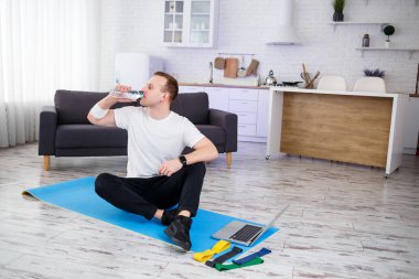 İnternetteki eğitimden sonra mutlu genç adam su içiyor. Evde spor yapmak, sağlıklı bir yaşam tarzı.