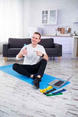 İnternetteki eğitimden sonra mutlu genç adam su içiyor. Evde spor yapmak, sağlıklı bir yaşam tarzı.