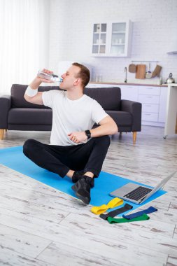 İnternetteki eğitimden sonra mutlu genç adam su içiyor. Evde spor yapmak, sağlıklı bir yaşam tarzı.