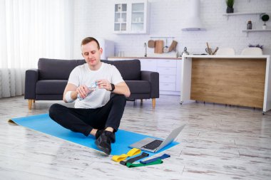 İnternetteki eğitimden sonra mutlu genç adam su içiyor. Evde spor yapmak, sağlıklı bir yaşam tarzı.