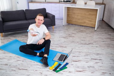 Adam spor için eve gidiyor. Sporcu evde yerde otururken su içer, sağlıklı bir yaşam tarzı.