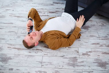 Oturma odasındaki kanepenin yanında yerde yatan ve dinlenen mutlu genç adam.