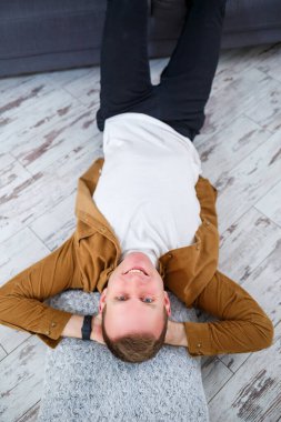 Oturma odasındaki kanepenin yanında yerde yatan ve dinlenen mutlu genç adam.