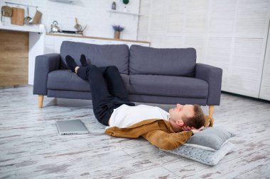 Çekici, güler yüzlü, gündelik giysili genç adam oturma odasındaki koltukta dizüstü bilgisayar kullanarak oturuyor.