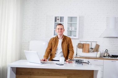 Mutfaktaki masada uzaktan kumandayla çalışan yakışıklı genç bir iş adamı. Odada oturan mutlu adam elinde bir dron tutuyor.