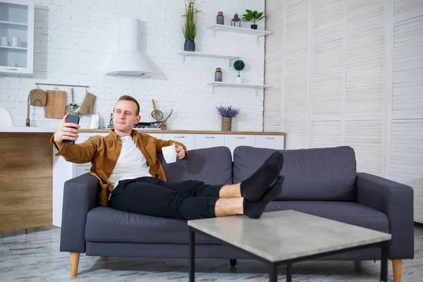 Genç ve başarılı bir adam evinde kanepede oturuyor elinde telefon ve video bağlantısı ile konuşuyor. Karantina sırasında uzak çalışma.