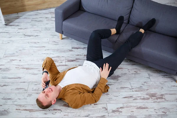 Oturma odasındaki kanepenin yanında yerde yatan ve dinlenen mutlu genç adam.