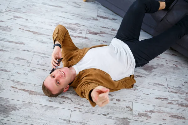 Oturma odasındaki kanepenin yanında yerde yatan ve dinlenen mutlu genç adam.