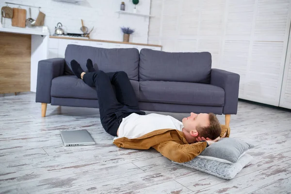 Çekici, güler yüzlü, gündelik giysili genç adam oturma odasındaki koltukta dizüstü bilgisayar kullanarak oturuyor.