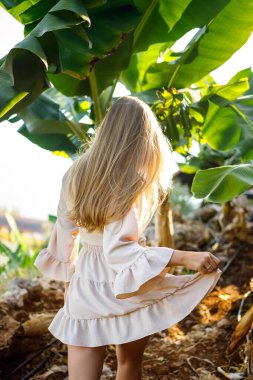 Parktaki bir muz ağacının büyük yeşil yaprağının yanında bir kadın. Tropik bitkiler ve yürüyen çekici bir kız.