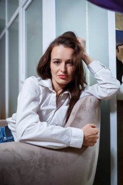 Genç, güzel, serbest çalışan bir kadın beyaz gömlekli bir sandalyede oturuyor. Çalışma gününde tatil.